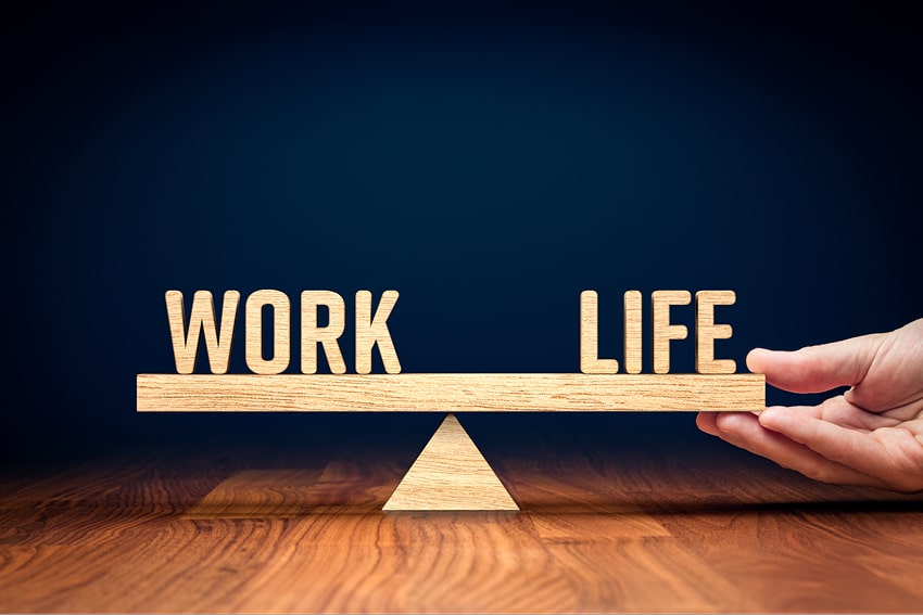 The words work and life balancing on a wooden scale